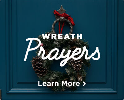 An Advent wreath decorated with a vibrant red bow and pinecones, hanging on a blue door. Image links to Advent Wreath Prayers page. 